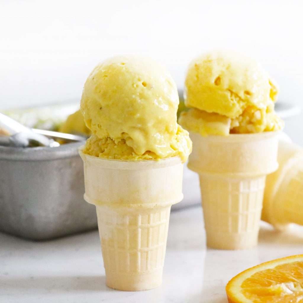 Two ice cream cones with a scoop of orange nice-cream.