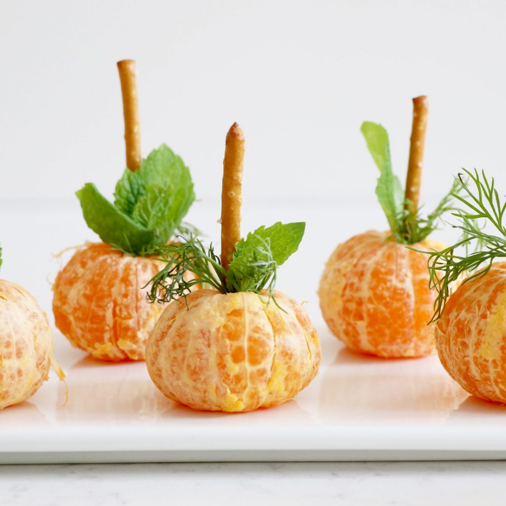 Oranges topped with pretzel and greens on white plate.