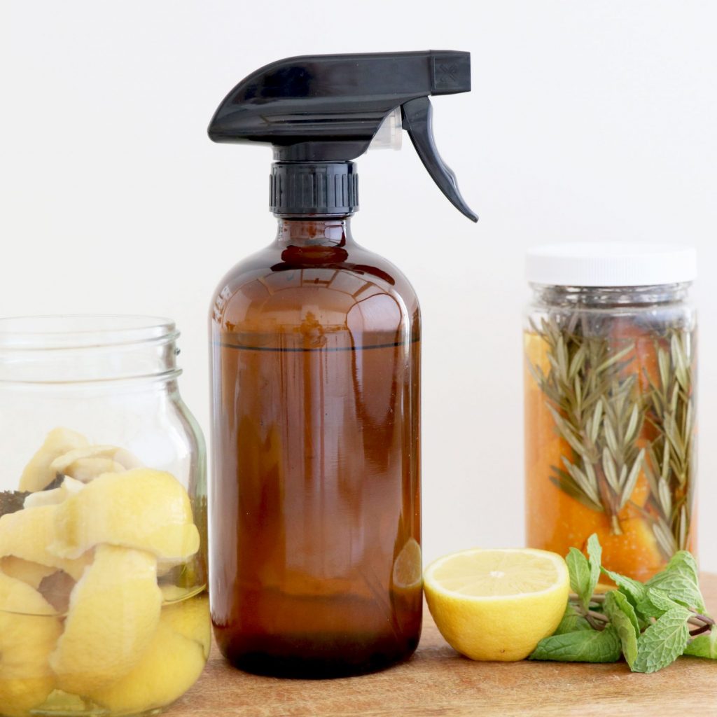 Sprayer bottle surrounded by mason jars filled with citrus and herbs.