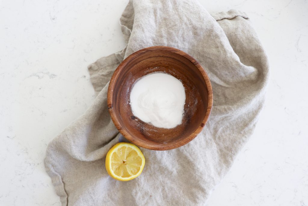 Wooden bowl with baking soda and juiced lemon on the side on a grey towel.